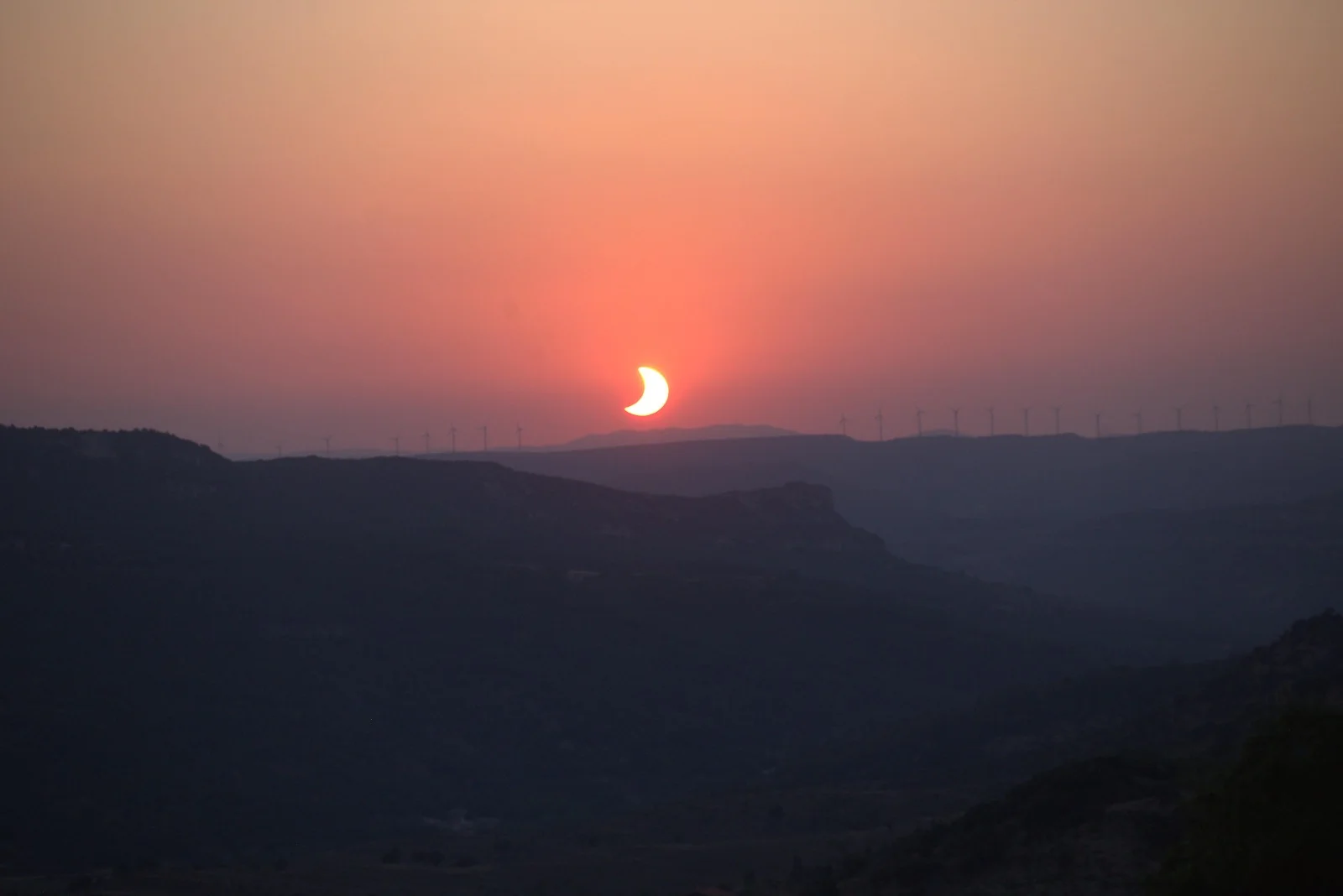 Tramonto con il Sole parzialmente eclissato sopra le pale eoliche